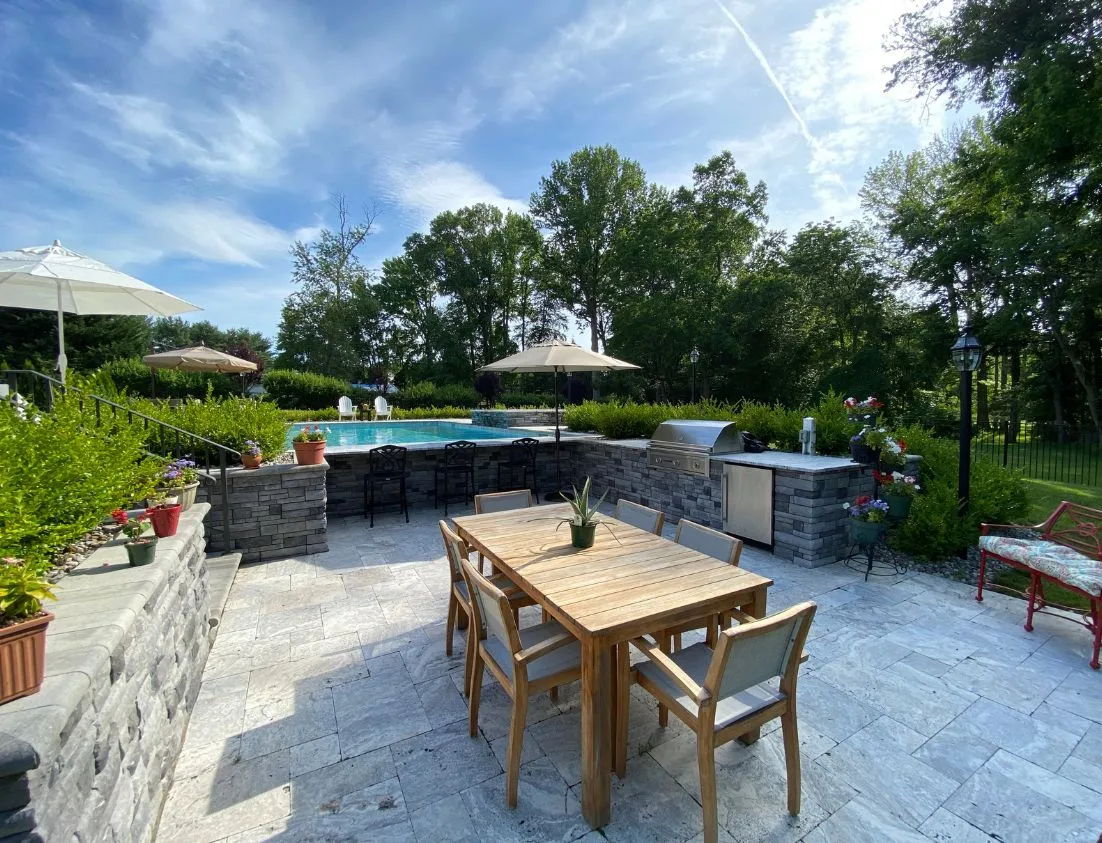 outdoor kitchen by inground pool with swim up bar and travertine patio build